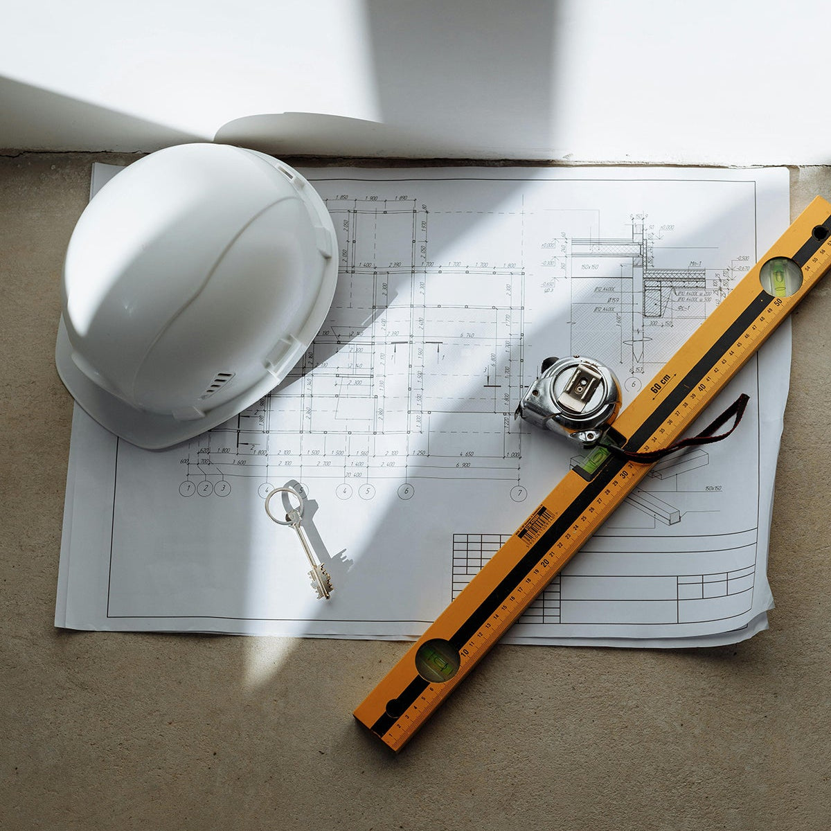 Construction helmet, wrench, level, and blueprints on a wooden surface